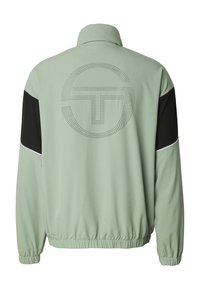 Lysegrønn jakke med svarte detaljer, elastiske mansjetter og ståkrage. Har en prikket sirkulær logo på baksiden.