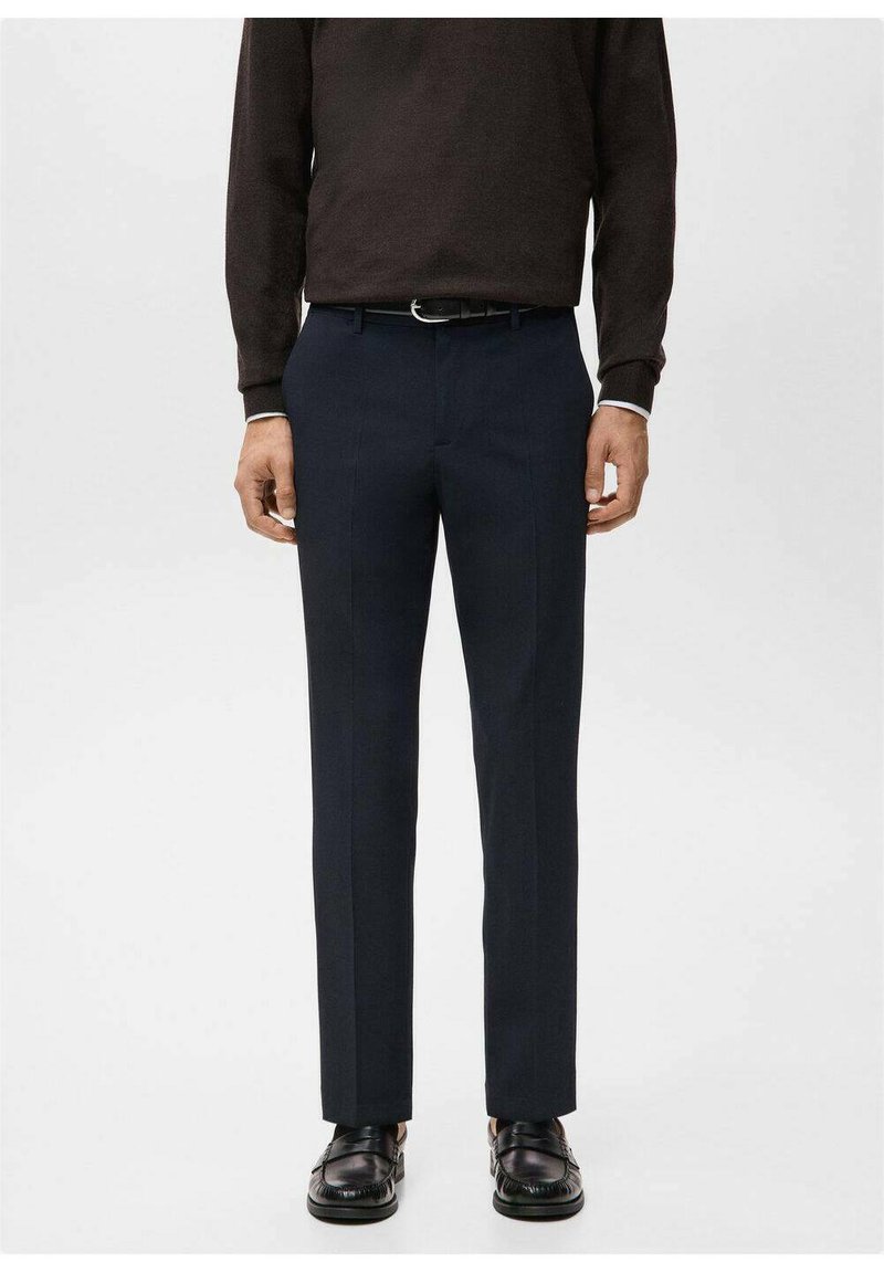 Granatowe spodnie na płaskim kroju z gładkiej tkaniny, z dopasowanym fasonem i kantem z przodu, noszone z brązowym swetrem i czarnymi butami.
