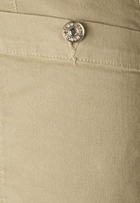 Beige puuvillakangas, jossa on vinoraitakuvio, accentoituna hopeisella metallinapilla ja näkyvällä ompeleella.
