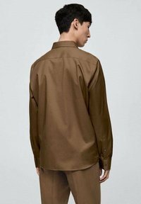 Camicia marrone a maniche lunghe dal taglio rilassato, con colletto classico, polsini con bottoni e texture liscia senza motivi visibili.