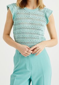 Ljusblå stickad topp med en texturerad, öppen vävdesign och korta ärmar, kombinerad med matchande ljusblå byxor.