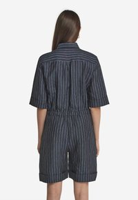 Jeansbyxdress med korta ärmar, insvängd midja och uppvikta ärmslut, med horisontella och vertikala vita randar på en mörkblå bakgrund.