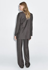 Gray tailored suit featuring a long blazer and wide-leg pants, made of textured fabric with button accents on the sleeves.