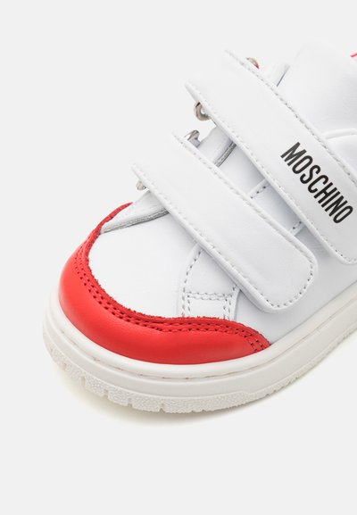 Valged tossud punaste aktsentidega, valmistatud sünteetilisest materjalist; sisaldavad kahte Velcro rihma ja tekstureeritud kummist talla. Tekst: "MOSCHINO."