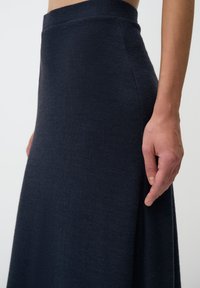 Jupe bleu marine en tissu texturé, ajustée à la taille et descendant jusqu'au sol, avec une finition lisse et un détail de couture latérale.