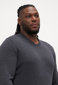 Maglione grigio antracite a V realizzato in tessuto a maglia, con maniche lunghe e un design aderente caratterizzato da una consistenza morbida.