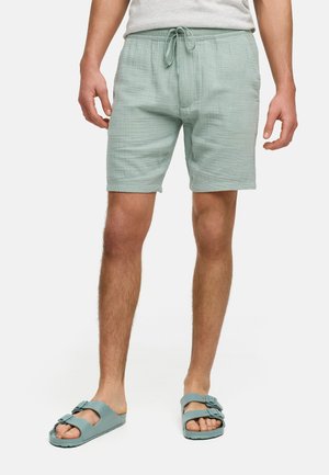 Lichtgroene, geweven shorts met een elastische tailleband en trekkoord. Gecombineerd met lichtblauwe slide-sandalen met dubbele gespen.