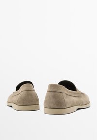 Mocassini in suede color taupe con punta rotonda, design slip-on e una suola in gomma minimale. Dettaglio di cuciture sul retro per un tocco di originalità.
