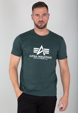 Dark green cotton t-shirt featuring a white logo with "ALPHA INDUSTRIES" text and a triangular design on the front. Short sleeves, crew neck.