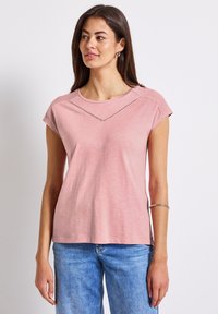 Růžové tričko s krátkým rukávem a kulatým výstřihem, které má textura podél ramenní části a volnější, pohodlný střih.