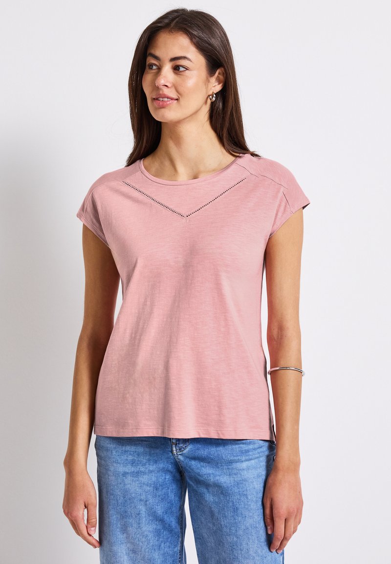 Růžové tričko s krátkým rukávem a kulatým výstřihem, které má textura podél ramenní části a volnější, pohodlný střih.