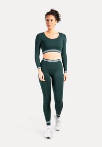 Donkergroen sportief set bestaande uit een crop top met lange mouwen en witte strepen, en een legging met hoge taille, met een gladde textuur en aansluitend ontwerp.