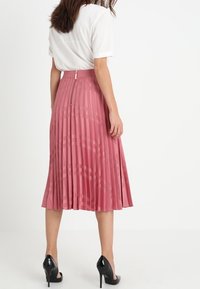Falda midi plisada rosa con cintura alta, tejido texturizado, cremallera oculta en la parte posterior y un acabado suave. Combinada con tacones negros.