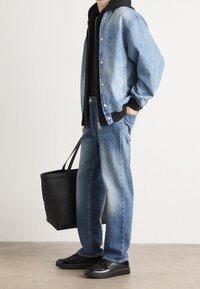 Light blue denim jacket over a black hoodie, paired with faded blue jeans and black sneakers. A black tote bag is held in one hand.