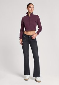 Fioletowa krótka kurtka na zamek z wysokim kołnierzem, zestawiona z ciemnymi dzwonami i białymi trampkami. Gładki materiał z subtelnymi detalami po bokach.