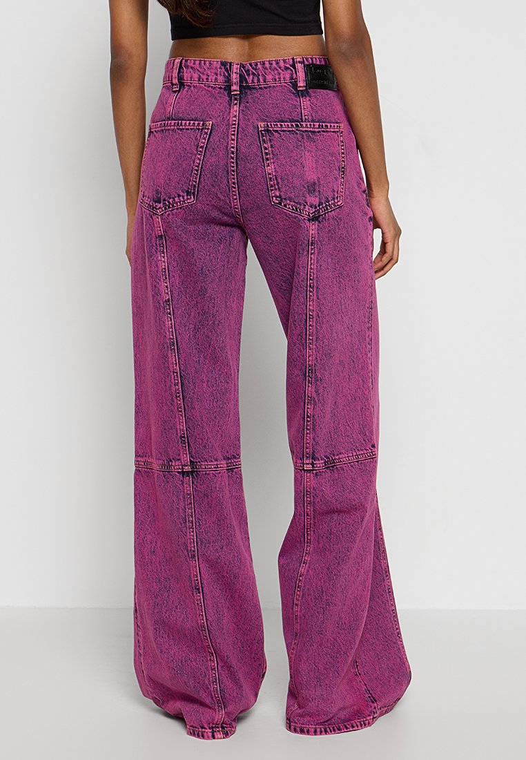 Pantaloni di jeans rosa a gamba larga con vita alta, due tasche posteriori e cuciture a contrasto. La texture è liscia con un leggero effetto lavato.