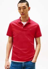 Κόκκινο πόλο μπλουζάκι από βαμβάκι, με κλασικό γιακά, δύο κουμπιά και μικρό λογότυπο στο αριστερό στήθος. Συνδυασμένο με μπλε τζιν.