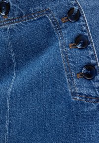 Jeanstyg med en medelblå tvätt och en slät struktur, fem stora svarta knappar längs sidan och kontrasterande orange sömmar.