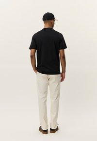 Black cotton t-shirt with short sleeves, plain design. Paired with light-colored trousers and a matching cap. Simple, casual look.