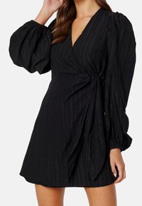 Vestido negro ajustado con textura acanalada, escote en V profundo y mangas abullonadas. Presenta un lazo lateral y un dobladillo acampanado, creando una silueta fluida.