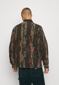 Camicia in velluto a coste con un motivo astratto nei toni del marrone, verde e beige, dalla vestibilità morbida e con polsini abbottonati.