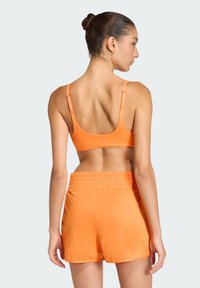 Sujetador deportivo naranja con tirantes ajustables, combinado con pantalones cortos naranja a juego que cuentan con una cinturilla elástica y una textura de tela suave.
