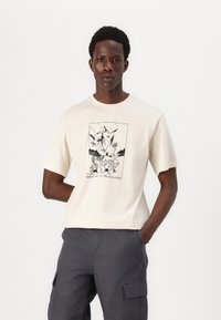 Cremefarvet bomulds t-shirt med et sort grafiktrykt motiv af dyr og landskaber. Kortærmet og med rund halsudskæring. Casual pasform.