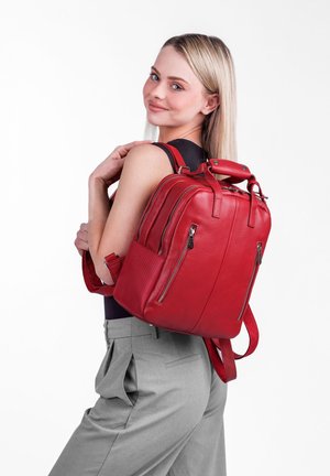 Roter Leder-Rucksack mit strukturierter Oberfläche, doppelten Reißverschlusstaschen vorne, Tragegriff oben und verstellbaren Schulterriemen. Der Hintergrund ist weiß.