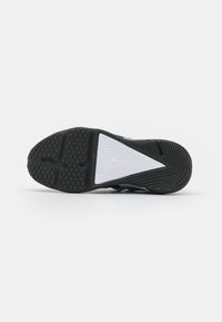 Semelle de chaussure de sport noire avec des motifs hexagonaux, accent triangulaire blanc, matériau en caoutchouc durable et surface texturée pour une traction.