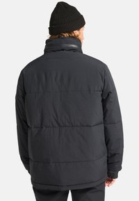 Czarna kurtka puchowa z pikowanymi sekcjami, wysokim kołnierzem i gładkim wykończeniem. W zestawie z teksturowanym czarnym beanie.