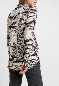 Langärmliges Hemd aus leichtem Stoff mit einer Mischung aus Leoparden- und Schlangenmustern in Beige, Schwarz und Braun, mit einem geknöpften Manschettenverschluss.
