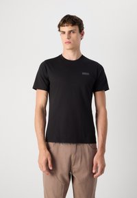Tricou negru din bumbac cu guler rotund și mâneci scurte; prezintă o mică etichetă de marcă pe partea stângă a pieptului.