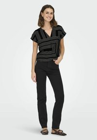 Top nero con strisce geometriche bianche, maniche corte e scollatura a V; abbinato a pantaloni neri slim-fit e scarpe flat.
