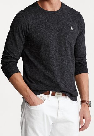 Langärmliges, dunkelgraues T-Shirt aus strukturiertem Stoff mit Rundhalsausschnitt und kleinem weißen Logo. Kombiniert mit weißen Hosen und einem braunen Gürtel.