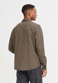 Bruine geweven shirt met een kraag, knopenmanchetten en een rechte zoom. Textuurstof en rugnaaddetails zichtbaar vanuit de achteransicht.