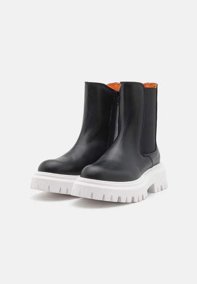 Botas de tobillo de cuero negro con cremallera lateral, con una suela de plataforma blanca gruesa y un forro interior naranja.
