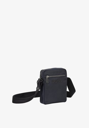 Mala cruzada preta em nylon com um bolso frontal com fecho. Apresenta um design plano, alça ajustável e logótipo em relevo na frente.