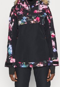 Anorak nero con motivo floreale, dotato di cappuccio rifinito in pelliccia, chiusura frontale con zip e maniche lunghe per una vestibilità comoda. Dettagli includono aperture per il pollice.