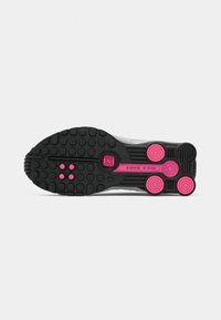 Sole butów biegowych Nike Shox w kolorze czarnym i różowym, pokazujący okrągłe wzory bieżnika oraz kolumny amortyzacyjne.