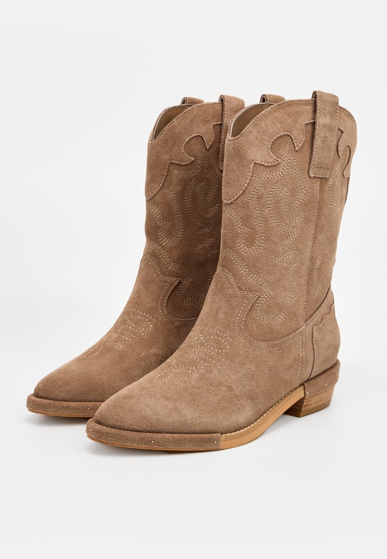 Botas de cowboy de ante marrón con costuras decorativas, punta afilada y tacón bajo apilado. Cuentan con lengüetas para facilitar el calce.