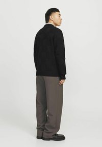 Melna adīta džemperis ar teksturētu šķērsojošo rakstu, kombinēts ar pelēkiem brīviem biksēm un melniem apaviem, skatīts no sāniem.