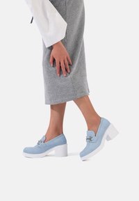 Scarpe platform azzurre in suede, con punta quadrata, tacco a blocco bianco e dettaglio in fibbia argentata. Texture liscia, design casual.