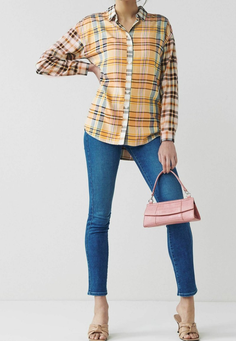 Camicia a maniche lunghe a quadri gialla, blu e arancione con chiusura a bottoni. Jeans skinny blu. Piccola borsa a tracolla rosa con finitura testurizzata.