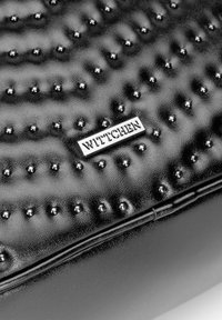 Bolso de cuero texturizado negro que cuenta con studs redondos elevados, un acabado suave y un logotipo metálico de WITTCHEN en la parte frontal.