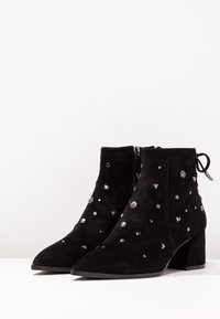 Stivaletti alla caviglia in suede nero con punta affusolata, decorati con borchie e forme metalliche, dotati di una zip laterale e di un tacco a blocco.