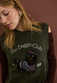Grön stickad väst med broderad taxdesign och randig tröja. Texten lyder "The Doggie Club" med åren 1971 och 1994.