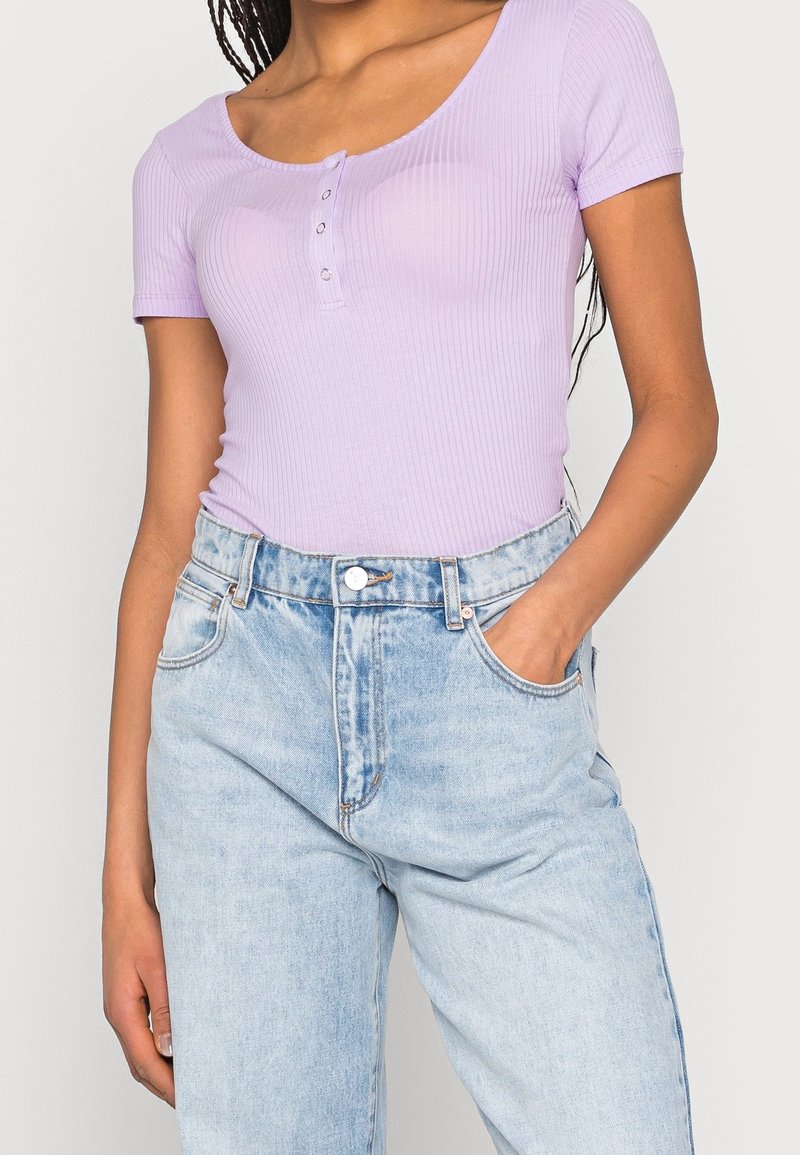 Ljuslila ribbad kortärmad bodysuit med rundad halsringning och tre knappar, i kombination med högmidjade ljusblå denimjeans.