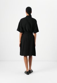 Black dress with short sleeves and a belt at the waist, made of soft fabric, falling just above the knee, with a relaxed silhouette.