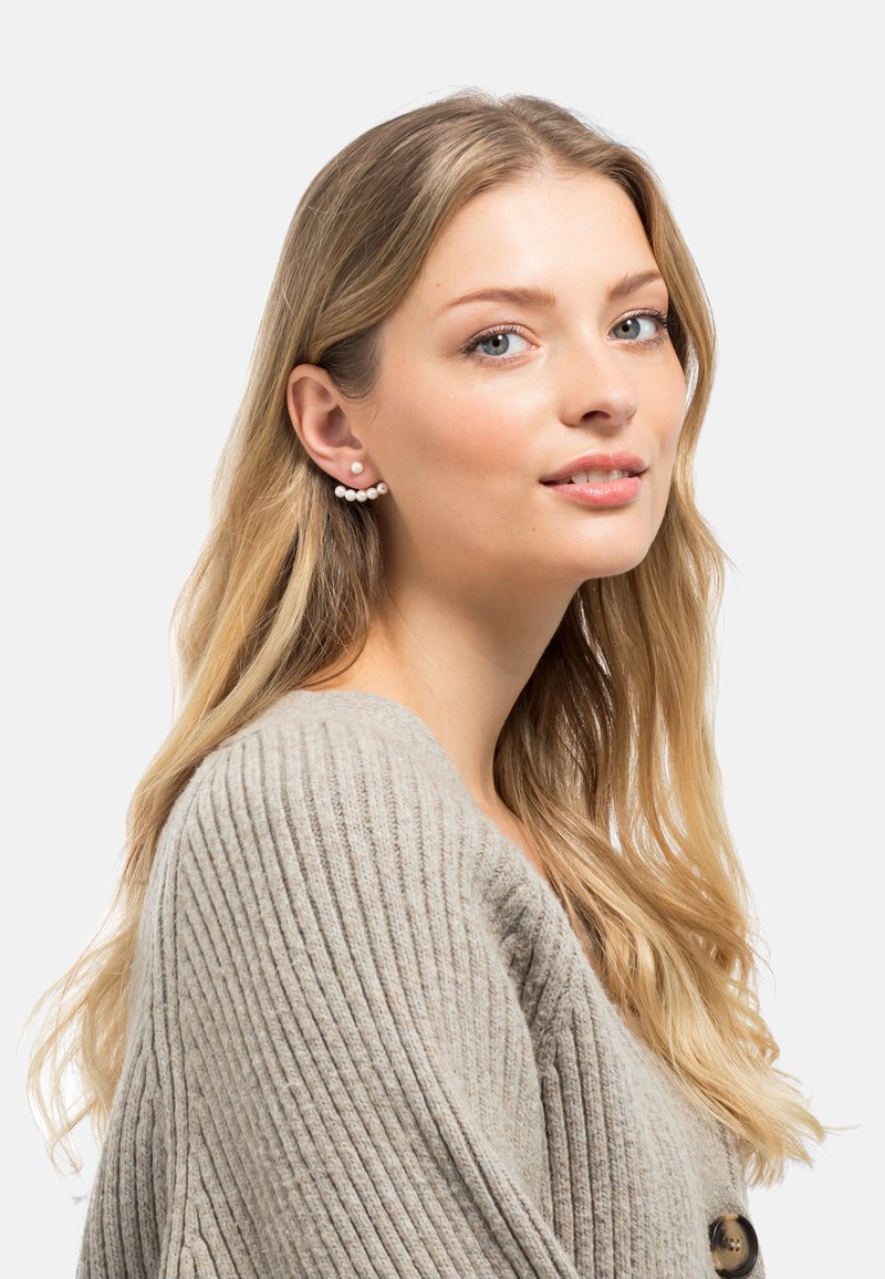 Silberfarbene Ohrringe mit einer Reihe kleiner Perlen und einem einzelnen Perlenstecker, präsentiert an einem Model mit langen blonden Haaren in einem gerippten Pullover.