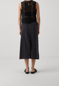 Top in pizzo nero con apertura a goccia sul retro, abbinato a una lunga gonna di jeans nera con orlo sfrangiato e due tasche posteriori. Indossato con sandali neri.